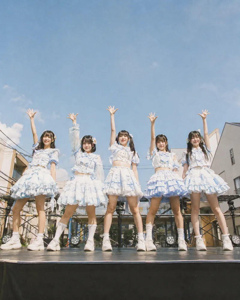 屋外ステージで手を上げる5人組アイドル