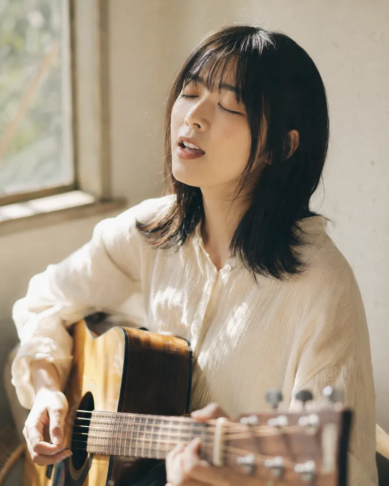 窓辺でアコースティックギターを弾き語る女性