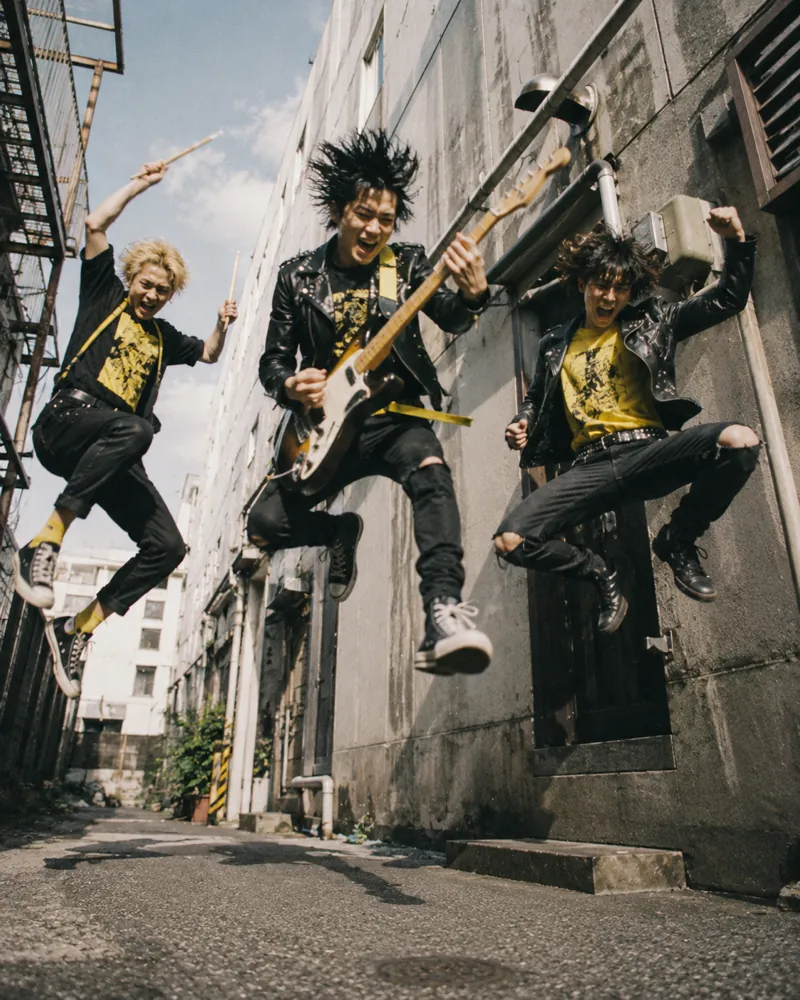 路地でジャンプする3人組パンクバンド